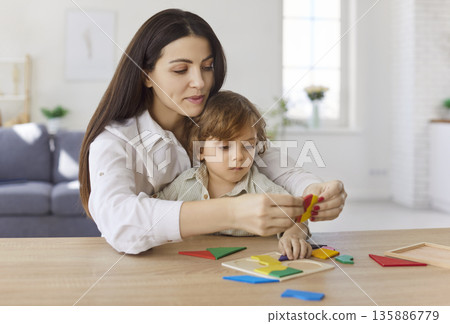Mother and child assembling colorful tangram puzzle at home, hands-on learning 135886779