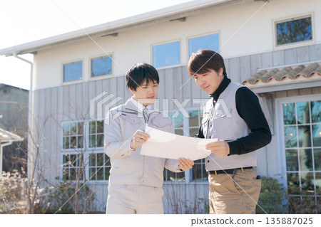 Craftsmen looking at blueprints in front of a house Craftsmen looking at blueprints in front of a house 135887025