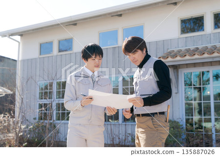 Craftsmen looking at blueprints in front of a house Craftsmen looking at blueprints in front of a house 135887026