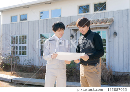 Craftsmen looking at blueprints in front of a house Craftsmen looking at blueprints in front of a house 135887033