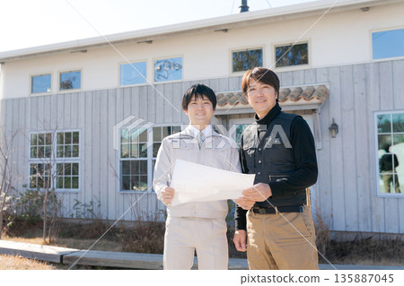 Craftsmen looking at blueprints in front of a house 135887045
