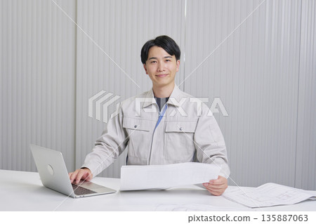 A man working at a construction company sitting with a blueprint, indoor portrait, looking at the camera A man working at a construction company sitting with a blueprint, indoor portrait, looking at the camera 135887063