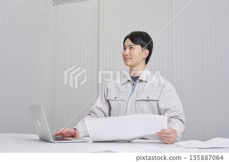 A man working at a construction company sitting with a blueprint, indoor portrait A man working at a construction company sitting with a blueprint, indoor portrait 135887064