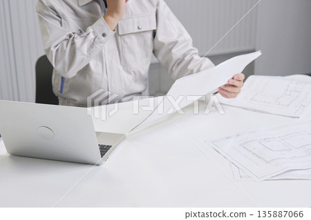 一個工人坐在辦公桌前，看著藍圖思考，面無表情。 135887066