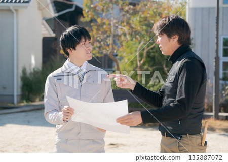 Craftsmen looking at blueprints in front of a house 135887072