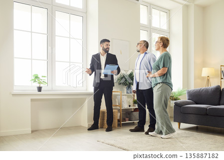 Realtor showing bright modern apartment interior to mature couple during tour 135887182