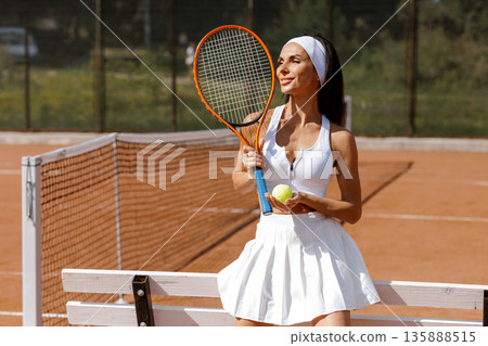 Female tennis player holds racket and ball near the net on clay court. Ideal for website banner or social ad about tennis training, fitness, and sport lifestyle. 135888515