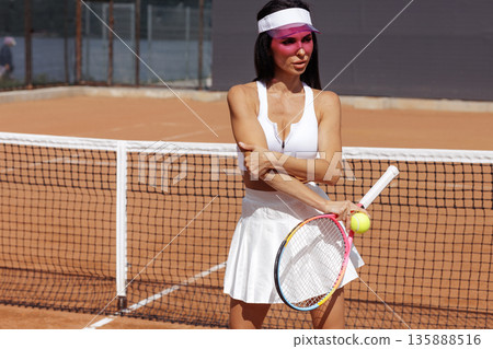 Female tennis athlete poses with racket and ball by the net on a clay court. Ideal for sports club website banner or social advertising. 135888516