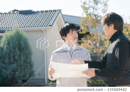 Craftsmen looking at blueprints in front of a house Craftsmen looking at blueprints in front of a house 135889482