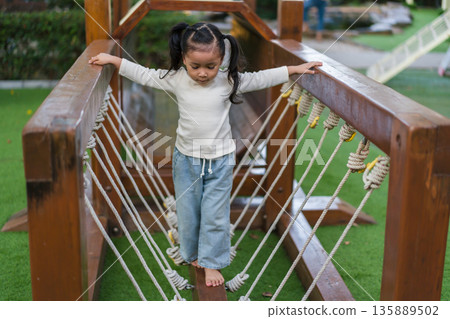 child girl playing and walking on wooden rope bridge at a outdoor playground in park child girl playing and walking on wooden rope bridge at a outdoor playground in park 135889502