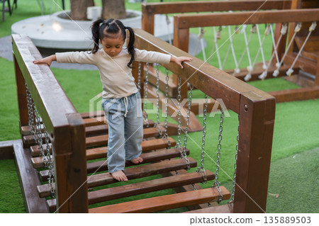 child girl playing and walking on wooden rope bridge at a outdoor playground in park child girl playing and walking on wooden rope bridge at a outdoor playground in park 135889503