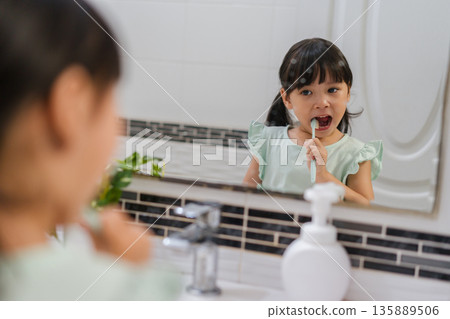 girl child brushing teeth at reflection in mirror in bathroom 135889506