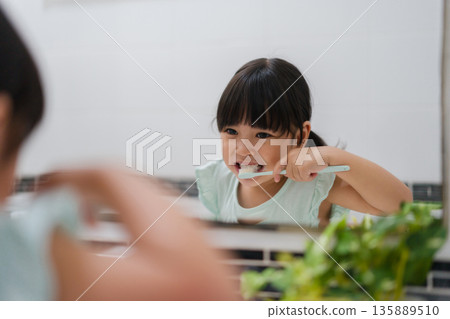 girl child brushing teeth at reflection in mirror in bathroom 135889510