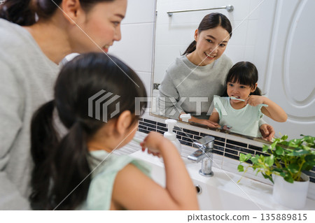 mother teaching girl child to brushing teeth at reflection in mirror in bathroom mother teaching girl child to brushing teeth at reflection in mirror in bathroom 135889815