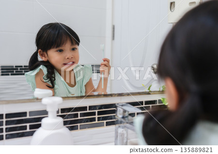 girl child brushing teeth at reflection in mirror in bathroom 135889821