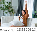 Happy young asian woman relax on comfortable couch at home texting messaging on smartphone 135890313