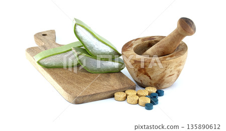 Aloe vera slices and pills next to a wooden mortar and pestle on a cutting board Aloe vera slices and pills next to a wooden mortar and pestle on a cutting board 135890612