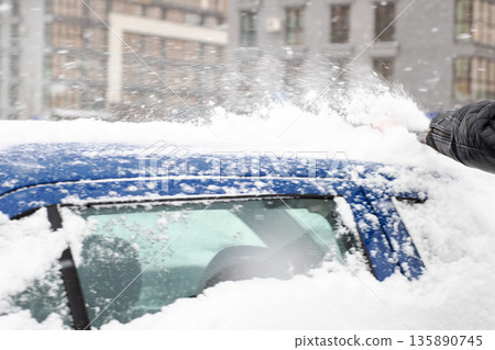 Clearing snow for safe visibility, Person removes thick snow from vehicle in winter conditions 135890745