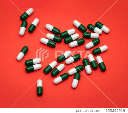 Pile of green and white capsules drugs on red background Pile of green and white capsules drugs on red background 135890919