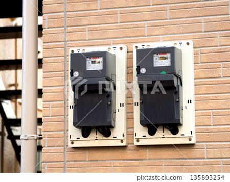 Two electric meters installed on the exterior wall of a house 135893254