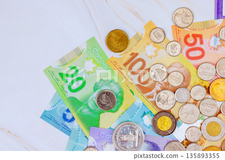 Several Canadian banknotes, coins are spread out on flat surface their different designs colors. Several Canadian banknotes, coins are spread out on flat surface their different designs colors. 135893355