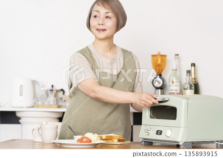 Senior woman toasting bread and eating breakfast in the kitchen Senior woman toasting bread and eating breakfast in the kitchen 135893915