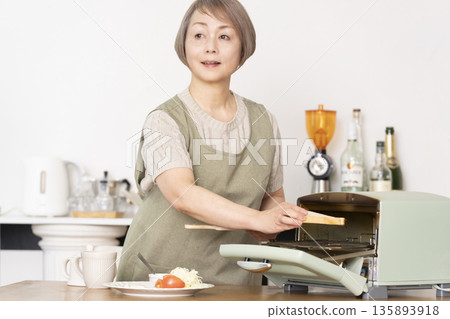 一位老婦人在廚房裡烤麵包吃早餐。 135893918