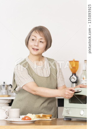 一位老婦人在廚房裡烤麵包吃早餐。 一位老婦人在廚房裡烤麵包吃早餐。 135893925