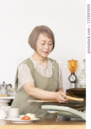 Senior woman toasting bread and eating breakfast in the kitchen 135893926