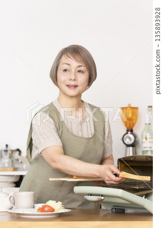 一位老婦人在廚房裡烤麵包吃早餐。 135893928