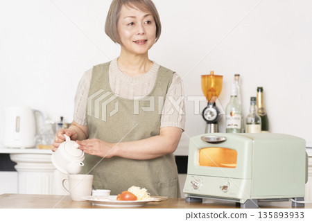 Senior woman toasting bread and eating breakfast in the kitchen Senior woman toasting bread and eating breakfast in the kitchen 135893933