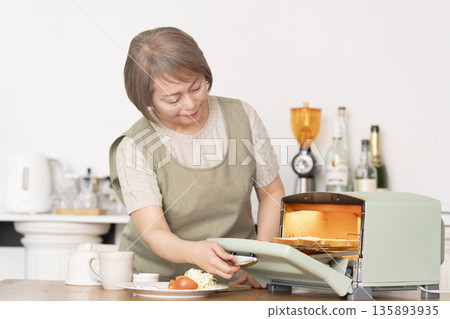 一位老婦人在廚房裡烤麵包吃早餐。 135893935