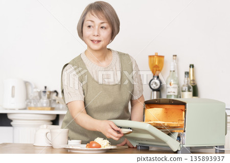Senior woman toasting bread and eating breakfast in the kitchen 135893937