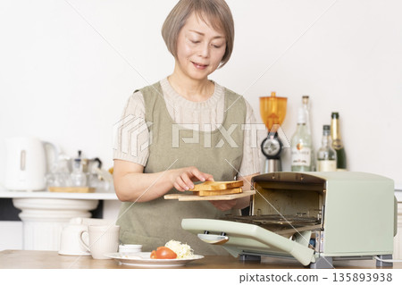 一位老婦人在廚房裡烤麵包吃早餐。 135893938