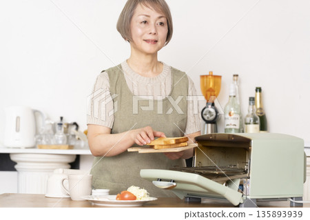 一位老婦人在廚房裡烤麵包吃早餐。 135893939