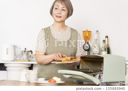 一位老婦人在廚房裡烤麵包吃早餐。 135893940