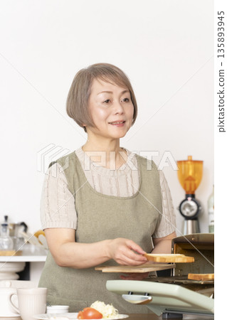 一位老婦人在廚房裡烤麵包吃早餐。 135893945