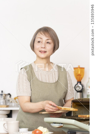 一位老婦人在廚房裡烤麵包吃早餐。 一位老婦人在廚房裡烤麵包吃早餐。 135893946