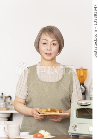 一位老婦人在廚房裡烤麵包吃早餐。 一位老婦人在廚房裡烤麵包吃早餐。 135893947
