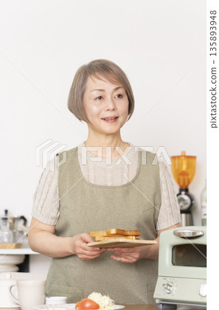 一位老婦人在廚房裡烤麵包吃早餐。 135893948