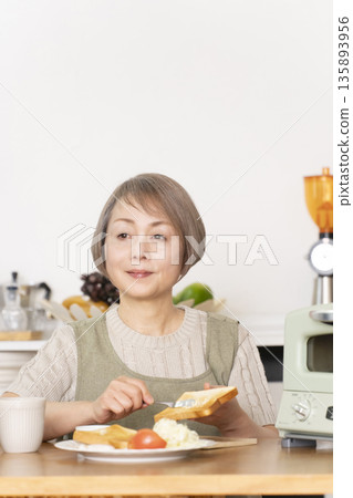 Senior woman toasting bread and eating breakfast in the kitchen 135893956