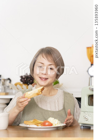 一位老婦人在廚房裡烤麵包吃早餐。 135893960