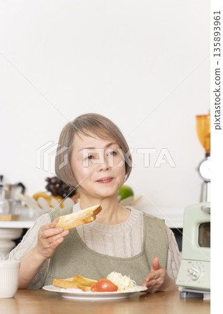一位老婦人在廚房裡烤麵包吃早餐。 135893961