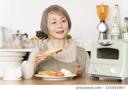一位老婦人在廚房裡烤麵包吃早餐。 135893967