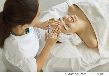 Head massage, facial spa treatment, anti age procedure for clients skin by cosmetologist, top view Head massage, facial spa treatment, anti age procedure for clients skin by cosmetologist, top view 135894069