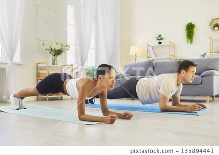 Couple holding forearm plank together at home, fitness training on yoga mats Couple holding forearm plank together at home, fitness training on yoga mats 135894441