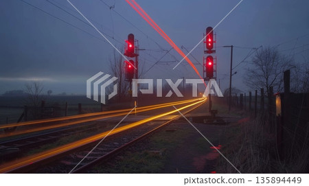 The humble train crossing in the rural countryside becomes a picturesque moment with light trails from passing cars 135894449