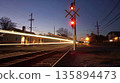 The passing lights of a train illuminate the quaint rural town as it crosses a peaceful train crossing 135894473
