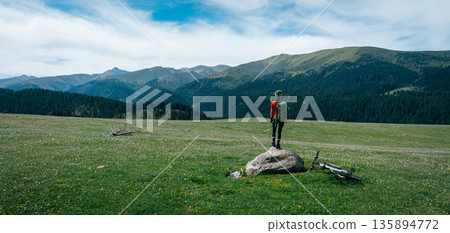 Aerial view of woman cyclist with mountain bike on flowering grassland mountain Aerial view of woman cyclist with mountain bike on flowering grassland mountain 135894772
