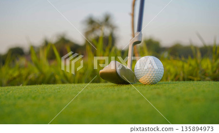 Golf clubs and balls on a green lawn in a beautiful golf course with morning sunshine. Golf clubs and balls on a green lawn in a beautiful golf course with morning sunshine. 135894973